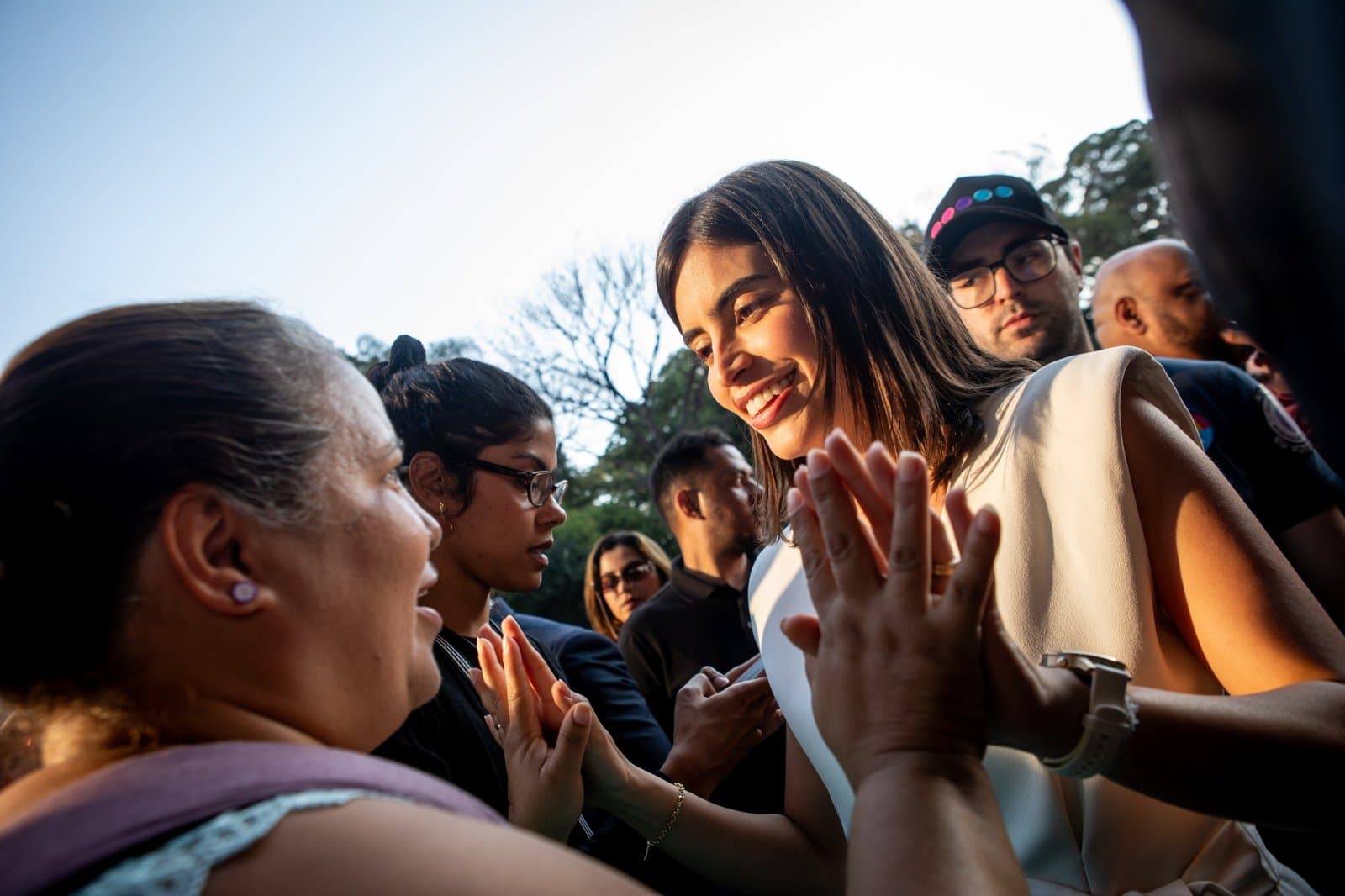 Tabata sorrindo e cumprimentando apoiadoras de mãos dadas durante agenda de rua